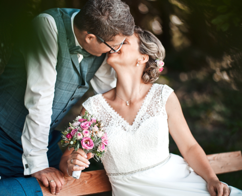 Hochzeitsbild von Brautleuten küssend auf einer Bank